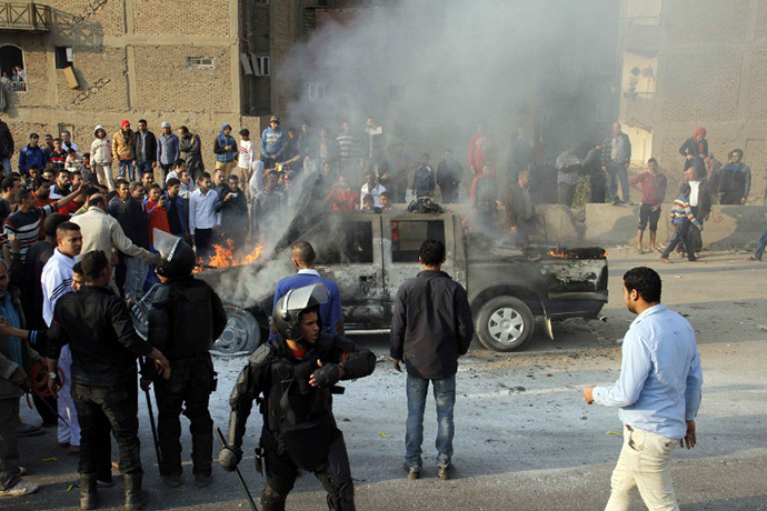 Egyptians look at a police vehicle set on fire by Muslim Brotherhood supporters on a ring road in the capital, Cairo, on January 3, 2014 as thousands of protesters backing deposed president Mohamed Morsi rallied across the country before police moved in to disperse them, sparking clashes. (AFP Photo / Khaled Kamel)