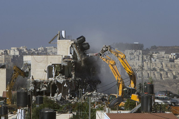 An Israeli municipality worker uses a mechanical shovel to demolish a house, belonging to a Palestinian family, that was built without municipal permission in the Arab east Jerusalem neighborhood of Beit Hanina on October 29, 2013. In the background is the Israeli settlement of Ramat (AFP Photo / Ahmad Gharabli)