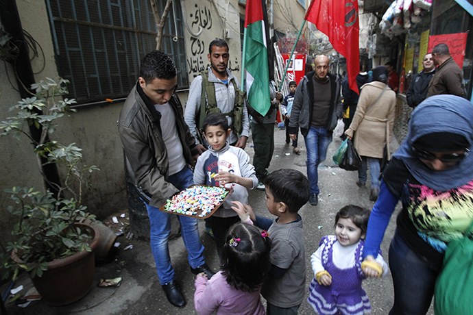 Palestinian refugees living in the the Shatila refugee camp in the Lebanese capital, had out sweets as they celebrate following the news of the death of former Israeli premier Ariel Sharon, on January 11, 2014. (AFP Photo / Anwar Amro)