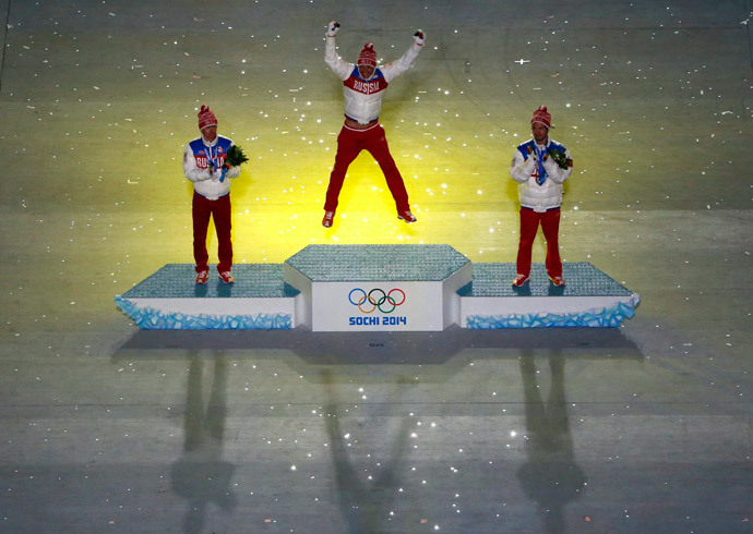 Gold medalist Alexander Legkov jumps on the podium beside silver medalist Maxim Vylegzhanin (L) and bronze medalist Ilia Chernousov (R), all of Russia, after they were presented with their medals in the men's cross-country 50 km mass start free event during the closing ceremony for the 2014 Sochi Winter Olympics, February 23, 2014. (Reuters / Eric Gaillard)