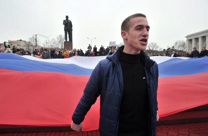 A pro-Russian activist holds part of a giant Russian flag near a statue of Lenin during a rally in Simferopol, the administrative center of Crimea, on March 1, 2014. (AFP Photo)