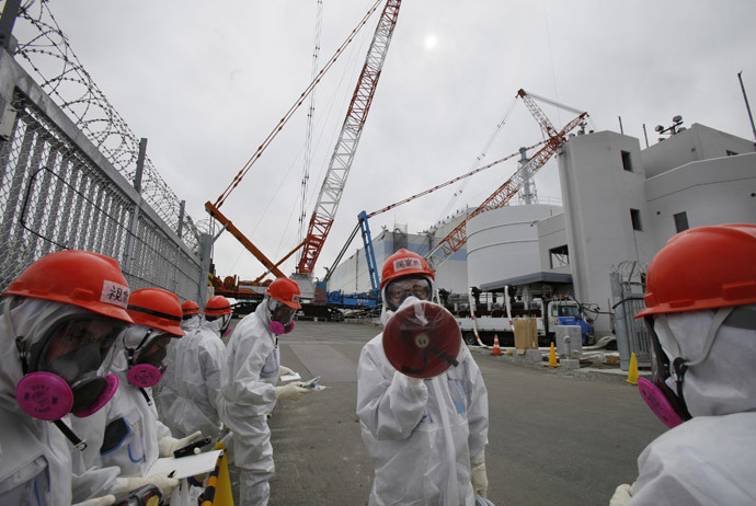 An employee (C) of Tokyo Electric Power Co. (TEPCO), wearing a protective suit and a mask, gives an explanation in front of No. 1 reactor building at the Tokyo Electric Power Co's (TEPCO) tsunami-crippled Fukushima Daiichi nuclear power plant in Fukushima prefecture March 10, 2014. (Reuters / Koji Sasahara / Pool)