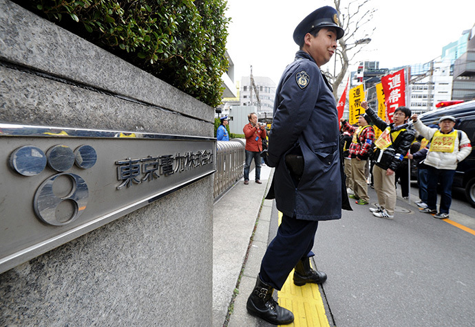 Security stands outside as Fukushima nuclear workers (behind) and their supporters shout slogans and raise their fists in front of the headquarters of Tokyo Electric Power Company (TEPCO), operator of the tsunami-battered Fukushima Daiichi nuclear power plant, during a rally in Tokyo on March 14, 2014 (AFP Photo / Toru Yamanaka)