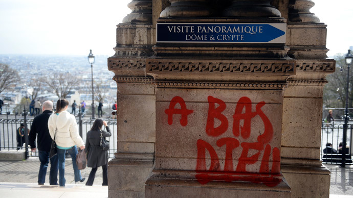 People walk past grafittis reading "Down with god" written on the Sacre-Coeur Basilica in the Montmartre area in Paris on March 19, 2014.(AFP Photo / Martin Bureau)