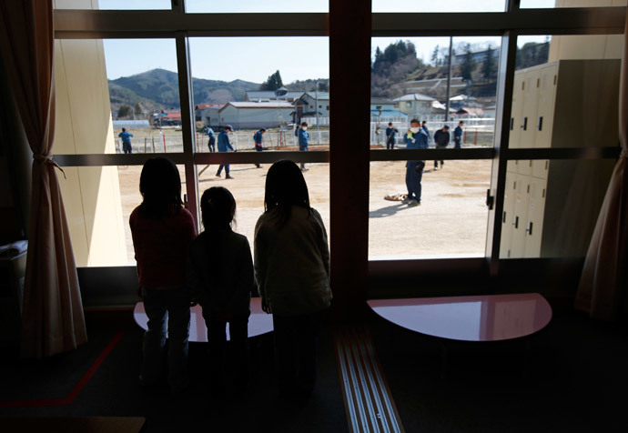 Children look through windows at their playground as the tsunami-crippled Fukushima Daiichi nuclear power plant operator Tokyo Electric Power Co. (TEPCO) volunteers removed ice and snow and levelled dirt in the ground, at a Miyakoji child care center at Miyakoji area in Tamura, Fukushima prefecture, April 1, 2014. (Reuters / Issei Kato)