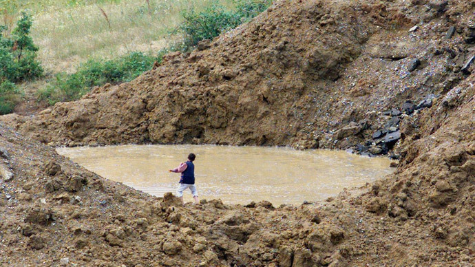 A Kosovar boy throws stones in a the flooded crater of bomb dropped during NATO strikes against Yugoslavia 01 July 1999 on a road between Malisevo and Pristina, southwestern Kosovo.(AFP Photo / Jean-Philippe Ksiazek)