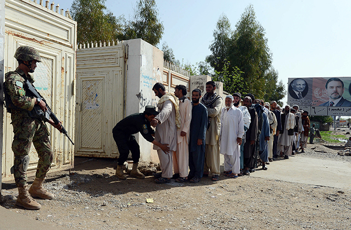 An Afghan soldier (L) watches as a policeman searches voters prior to entering a local polling station to cast their vote in Kandahar on April 5, 2014. (AFP Photo / Banaras Khan)
