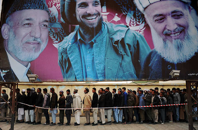 Afghan residents wishing to vote line up underneath a billboard showing images of Afghan President Hamid Karzai (L) and of deceased Afghan figures Burhandin Rabani (R) and Ahmad Shah Massoud (C) outside a polling station in Mazar-i-Sharif on April 5, 2014. (AFP Photo / Farshad Usyan)