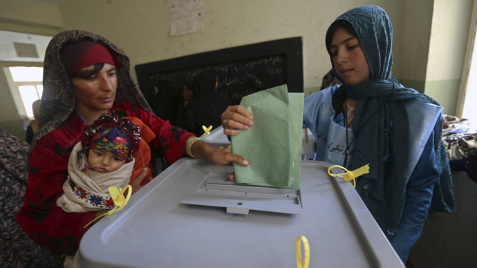 An Afghan woman carrying a child casts her vote at a polling station in Adraskan district, Herat province April 5, 2014. (Reuters/Omar Sobhani)