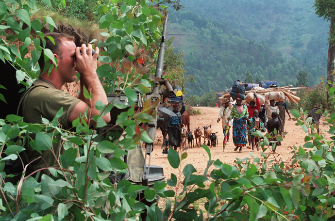 A French soldier who is hiding himself behind a tree looks through binoculars 12 July 1994 as Rwandan refugees are heading to the refugee camp of Kivumu, western Rwanda, to flee fighting between the Rwandan army and the National Liberation Front of Rwanda (AFP Photo)