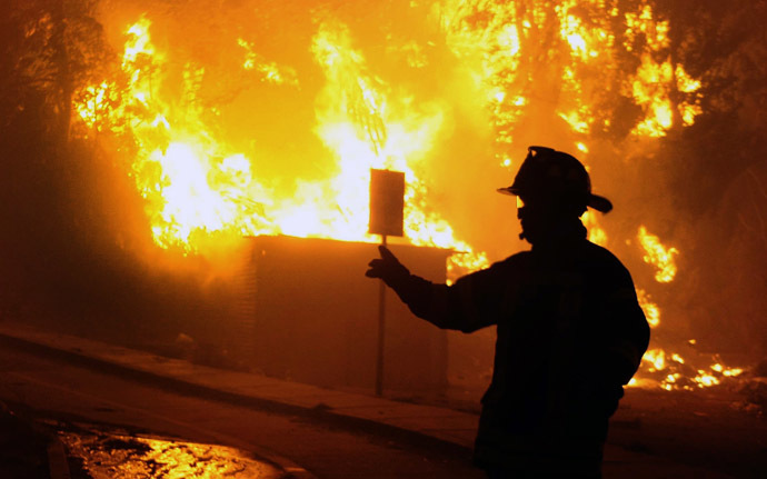 A firefighter stands next to burnig houses during a fire in Valparaiso, 110 km west of Santiago, Chile, on April 12, 2014. (AFP Photo/Felipe Gamboa)