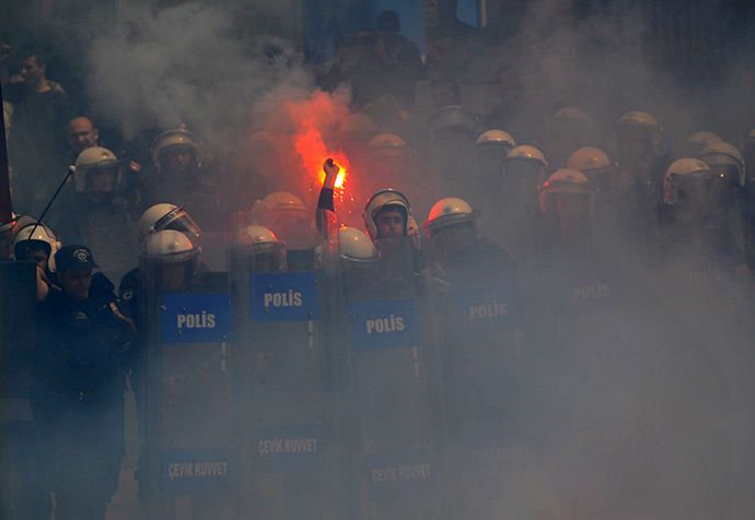 A Turkish police throws a flare back to football fans as they protest against a new system of e-tickets on April 20, 2014, on Istiklal Avenue in Istanbul. (AFP Photo / Ozan Kose)