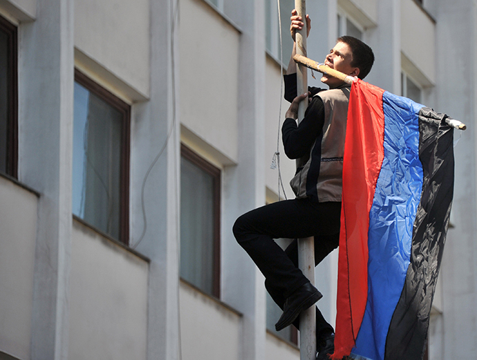 An activist climbs up on the flagpole as he holds flag of so-called Donetsk Republic in the teeth after Ukrainian policemen left their guarding outside of state city building in southern Ukrainian city of Mariupol on May 7, 2014. (AFP Photo / Genya Savilov)