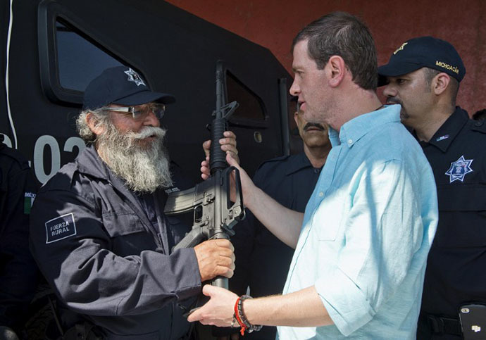 Estanislao Beltran (L), aka "Papa Pitufo" (Papa Smurf in English), leader of the local self-protection police, wearing his new uniform of the rural police, receives an AR-15 assault rifle from the Commissioner for Development and Security of Michoacan, Alfredo Castillo, in Tepalcatepec, Michoacan State, Mexico, on May 10, 2014.(AFP Photo / Ronaldo Schemidt)