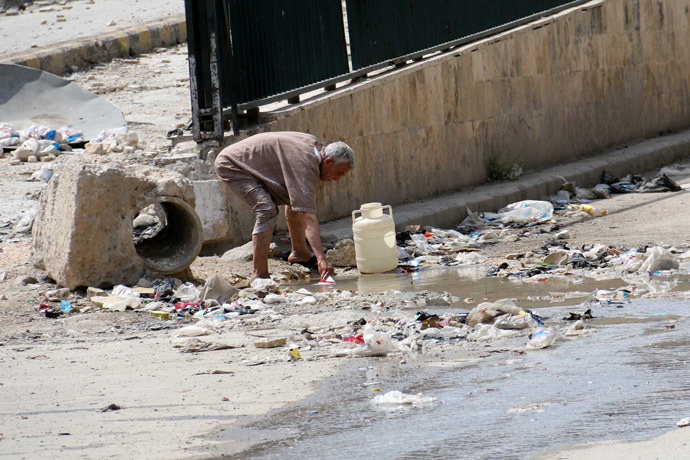 A man collects stagnant murky water from the side of a road in a rebel-held area in Aleppo on May 12, 2014. (AFP Photo/Zein Al-Rifai)