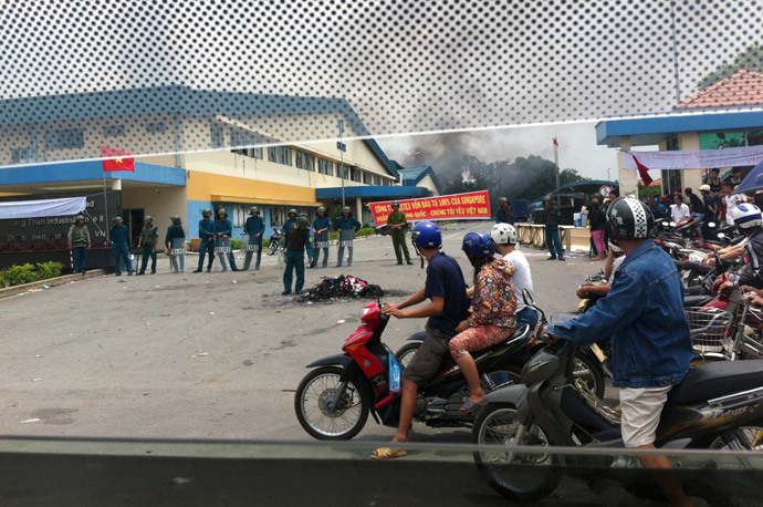 Commuters drive past as riot police (L) stand guard outside a burning factory building (back) in the Vietnamese southern province of Binh Duong on May 14, 2014.(AFP Photo / STR)