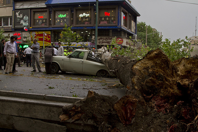 The trunk of a tree lies over a smashed vehicle following a sandstorm and record winds in Tehran on June 02, 2014. (AFP Photo / Str / Fars News)