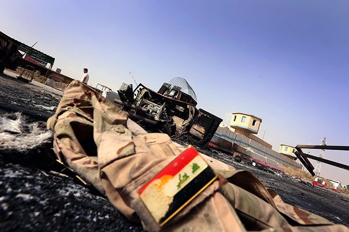 The jacket belonging to an Iraqi Army uniform lies on the ground in front of the remains of a burnt out Iraqi army vehicle close to the Kukjali Iraqi Army checkpoint, some 10km of east of the northern city of Mosul, on June 11, 2014. (AFP Photo / Safin Hamed)