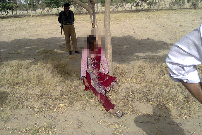A policeman stands near the body of Muzammil Bibi, 20, after policemen lowered her after she was found hanging from a tree in the town of Nawan Kot, located in Pakistan's Punjab province June 20, 2014. (Reuters / Irshad Hussain)