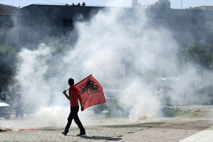 A Kosovo Albanian man, holding an Albanian flag, walks near tear gas fired by riot-police during clashes on June 22, 2014 in the divided town of Mitrovica. (AFP Photo / Armend Nimani)