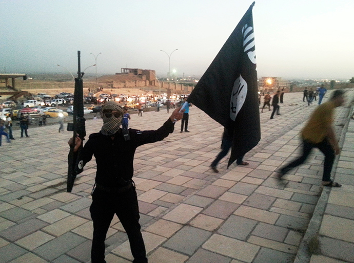 A fighter of the Islamic State of Iraq and the Levant (ISIL) holds an ISIL flag and a weapon on a street in the city of Mosul, June 23, 2014 (Reuters / Stringer)