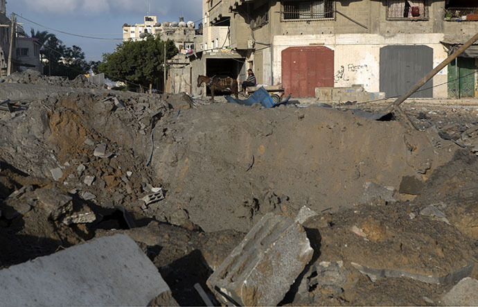 A Palestinian man rides a donkey cart past a crater following an overnight Israeli air strike, on July 3, 2014 in Gaza City. (AFP Photo / Mohammed Abed)
