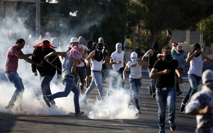 Palestinian protesters stand amid smoke after Israeli forces fired tear gas during clashes in Shuafat, East Jerusalem on July 4, 2014. (AFP Photo / Thomas Coex)