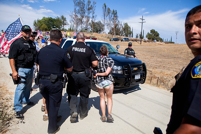 A protester is handcuffed and placed in a police car after a scuffle broke out before the possible arrivals of undocumented migrants who may be processed at the Murrieta Border Patrol Station in Murrieta, California July 4, 2014 (Reuters / Sam Hodgson)