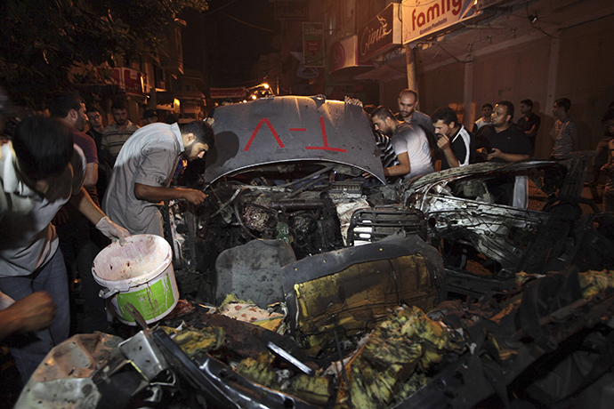 Palestinians inspect the remains of a car which police said was hit in an Israeli air strike in Gaza City July 9, 2014. (Reuters / Ashraf Amrah)