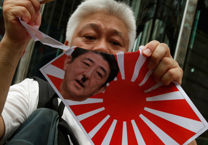 A protester tears an image of a Japanese military flag with a defaced portrait of Japanese Prime Minister Shinzo Abe, outside the Japanese consulate in Hong Kong July 7, 2014.(Reuters / Bobby Yip)