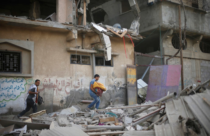 Palestinians carry their belongings as they walk amongst the debris of a house which police said was hit by an Israeli air strike in Gaza City July 15, 2014. (Reuters / Mohammed Salem)
