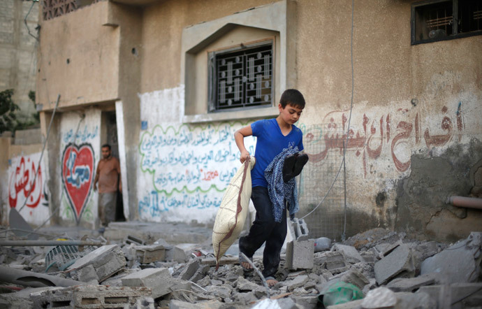 A Palestinian boy carries his belongings as he walks amongst the debris of a house which police said was hit by an Israeli air strike in Gaza City July 15, 2014. (Reuters / Mohammed Salem)