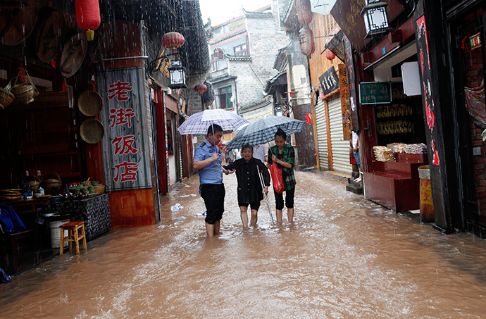 A police officer (L) helps an elderly woman evacuate from a flooded street of the ancient town as heavy rainfall hits Fenghuang county, Hunan province July 15, 2014 (Reuters / China Daily)
