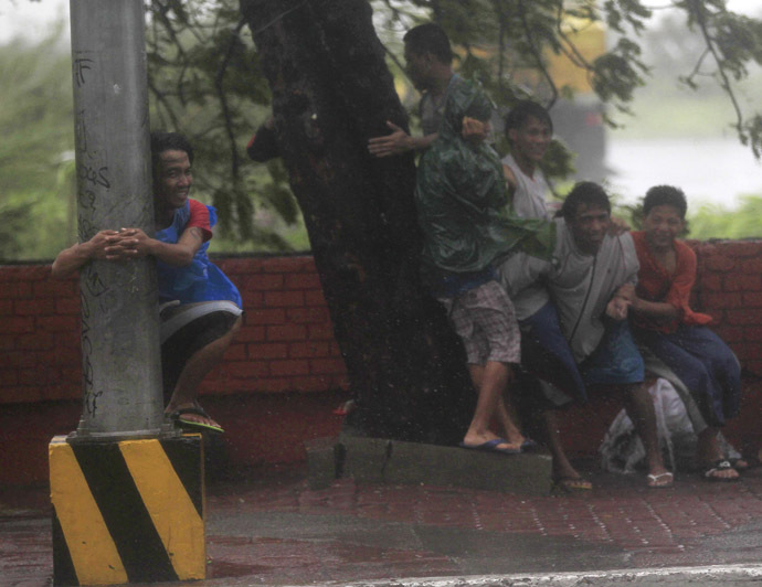 A boy hugs an electric post while other people take cover under a tree as strong winds brought by Typhoon Rammasun, locally called Glenda, battered the capital, metro Manila July 16, 2014. (Reuters)