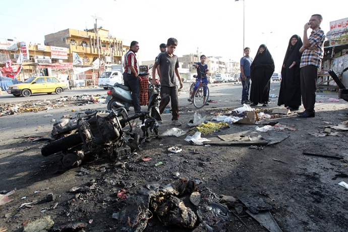 Iraqi onlookers gather on July 16, 2014 around a burnt motorcycle at the scene of an explosion that took place the previous night in Sadr City, one of Baghdad's northern Shiite-majority districts. (AFP Photo / Ali al-Saadi)