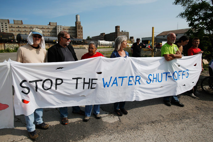 Protestors hold a banner across a drive way to block trucks from coming out of the gate of a private-contractor company hired to shut off the water to residential customers with unpaid bills in Detroit, Michigan July 18, 2014. (Reuters / Rebecca Cook)