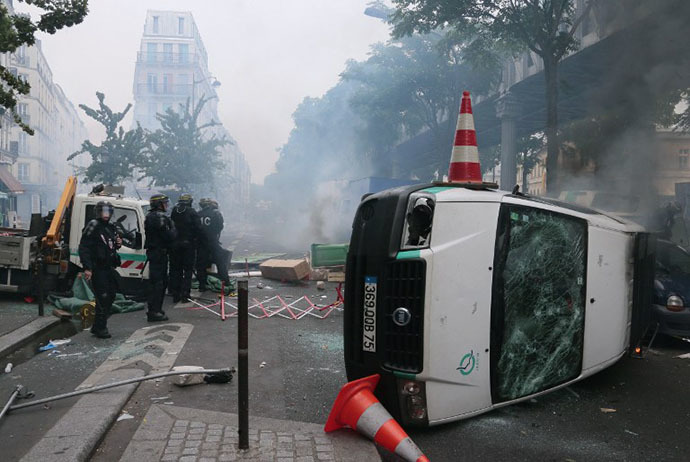 Riot police stand next to an overturned Paris public transport operator RATP van during clashes with protesters near the Barbes-Rochechouart aerial metro station in Paris on July 19, 2014. (AFP Photo / Jacques Demarthon)