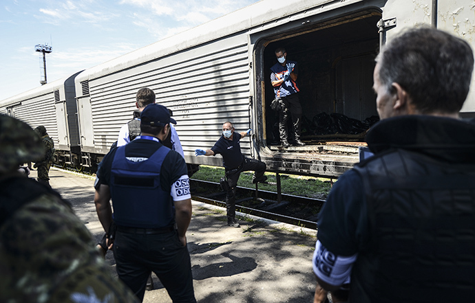 Monitors from the Organization for Security and Cooperation in Europe (OSCE) and members of a forensic team inspect a refrigerator wagon containing the remains of victims from the downed Malaysia Airlines Flight MH17, at a railway station in the eastern Ukrainian town of Torez on July 21, 2014. (AFP Photo / Bulent Kilic)