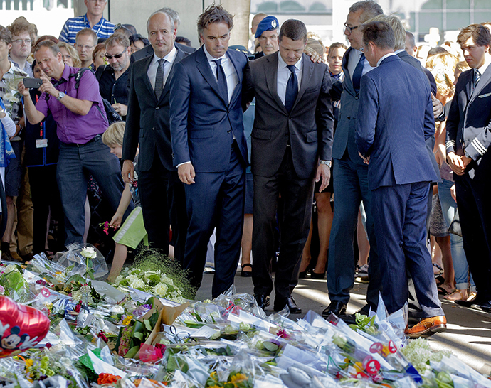 Deputy general director of Air France-KLM airline company Camiel Eurlings (2-L) and Chief Operating officer at KLM Pieter Elbers (3-R) stand in front of flowers laid for the victims of the downed Malaysia Airlines flight MH17 at the Schiphol Airport near Amsterdam, on July 23, 2014. (AFP Photo / Sander Koning)