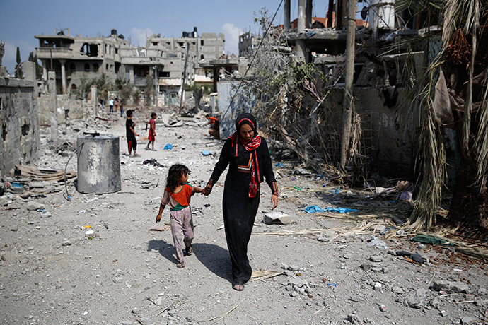 A Palestinian woman leads a girl past destroyed buildings after returning to Beit Hanoun town, which witnesses said was heavily hit by Israeli shelling and air strikes during the Israeli offensive, in the northern Gaza Strip August 5, 2014 (Reuters / Finbarr O'Reilly)