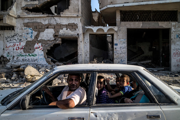 A Palestinian family drves past a destroyed building in the devastated neighbourhood of Shejaiya in Gaza City on August 6, 2014.(AFP Photo / Marco Longari)