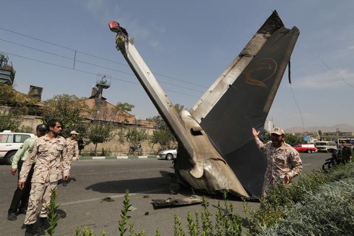 A member of the Iranian Revolutionary Guards reacts as he stands next to the remains of a plane that crashed near Tehran's Mehrabad airport on August 10, 2014. (AFP Photo / Atta Kenare)