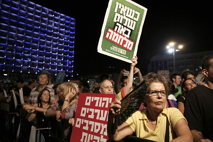 A demonstrator holds up placards reading in Hebrew: "When there is no peace war comes" (top) and "Jews and Arabs refuse to be enemies" (bottom) as thousands of Israelis protest during a left-wing peace rally in the coastal city of Tel Aviv calling for the Israeli government to negotiate with the Palestinian Authority on August 16, 2014. (AFP Photo / Gali Tibbon)