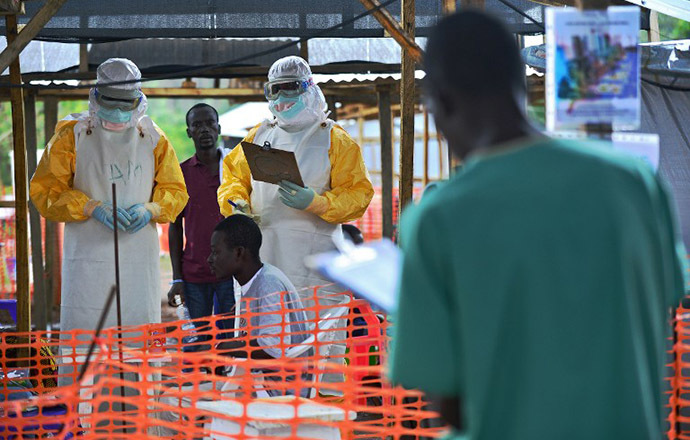 An MSF medical worker, wearing protective clothing relays patient details and updates behind a barrier to a colleague at an MSF facility in Kailahun, on August 15, 2014. (AFP Photo / Carl de Souza)