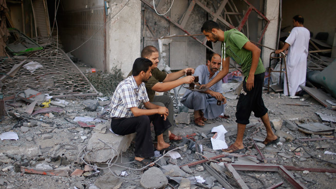 Palestinians drink coffee outside a damaged house as they look at the remains of a tower building housing offices, which witnesses said was destroyed by an Israeli air strike, in Gaza City August 26, 2014.(Reuters / Mohammed Salem)