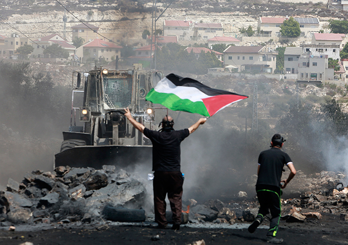 A protester holds a Palestinian flag in front of an Israeli army bulldozer during clashes following a protest against the nearby Jewish settlement of Qadomem, seen in the background, in the West Bank village of Kofr Qadom near Nablus September 5, 2014 (Reuters / Abed Omar Qusini)
