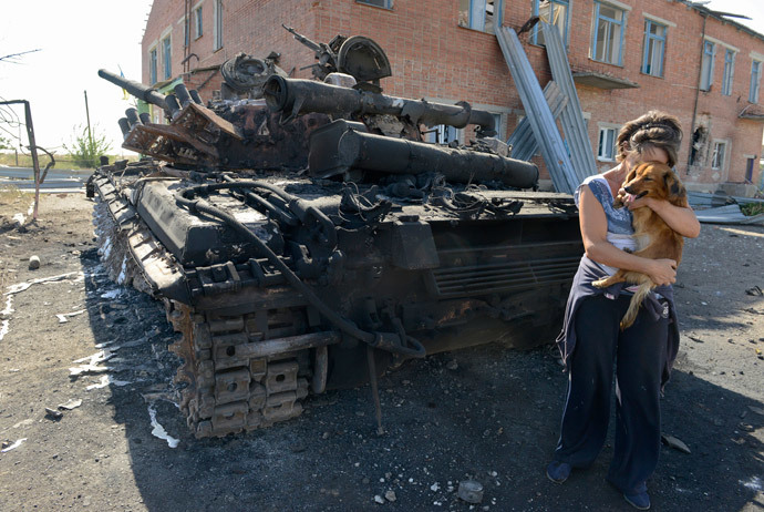 A woman holds a dog beside a destroyed tank in the courtyard of the local kindergarten in the village of Talakovka, some 22 kilometres northeast of Mariupol, on September 6, 2014.(AFP Photo / Alexander Khudoteply)