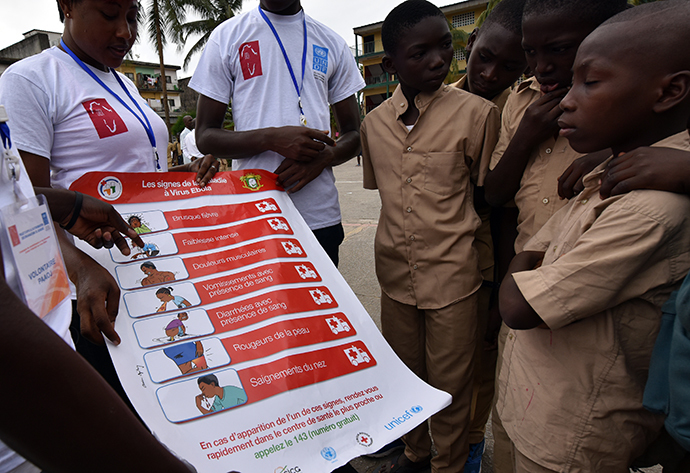 Volunteers wearing a t-shirt of the United Nations Development Programme (UNDP) show a placard to raise awareness on the symptoms of the Ebola virus to students of the Sainte Therese school, in the Koumassi district, in Abidjan (AFP Photo / Sia Kambou)