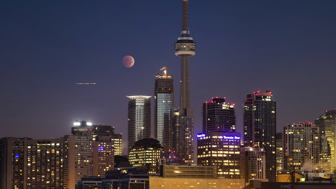 The moon turns orange during a total lunar eclipse behind the CN Tower and the skyline during moonset in Toronto October 8, 2014. (Reuters/Mark Blinch)