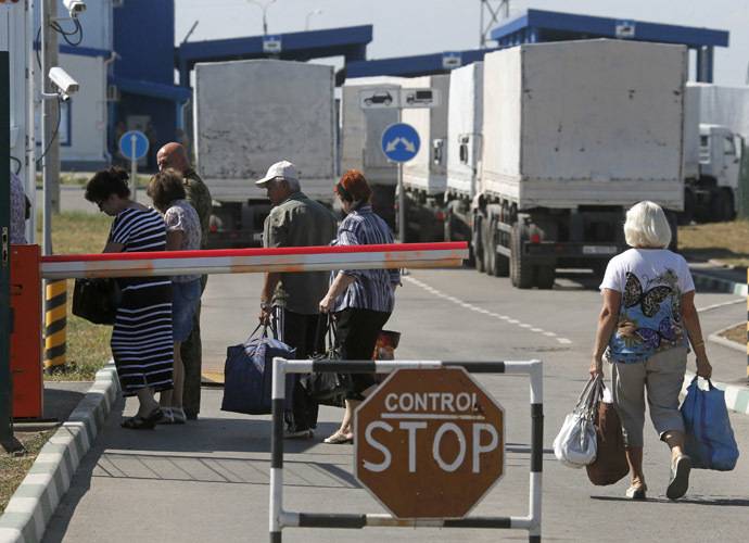Trucks of a Russian convoy carrying humanitarian aid for Ukraine are parked at a Russia-Ukraine border crossing point "Donetsk", with people crossing the border in the foreground, in Rostov Region, August 21, 2014. (Reuters/Alexander Demianchuk)